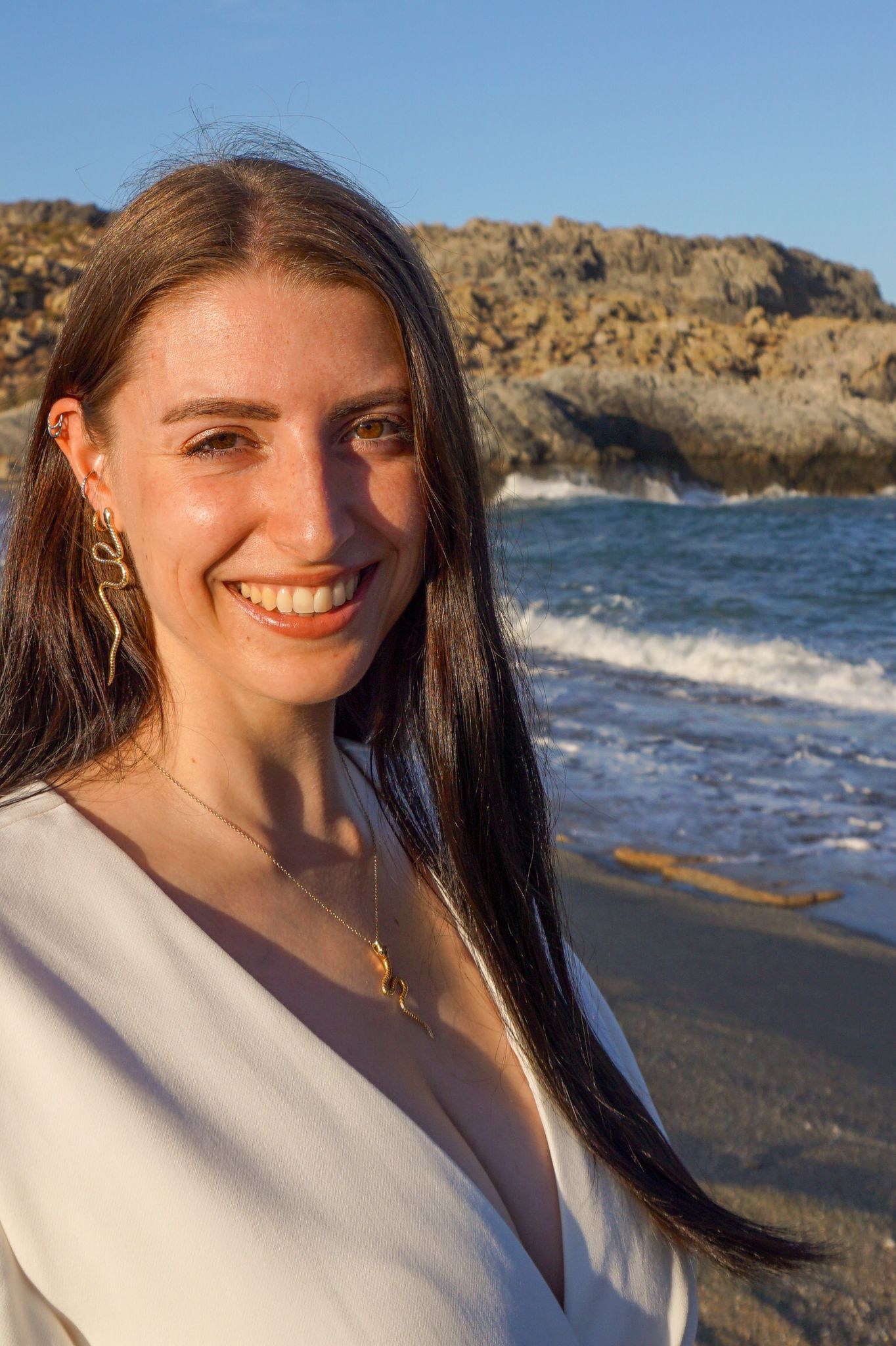 Anki at the sea wearing a white dress and smiling into the camera