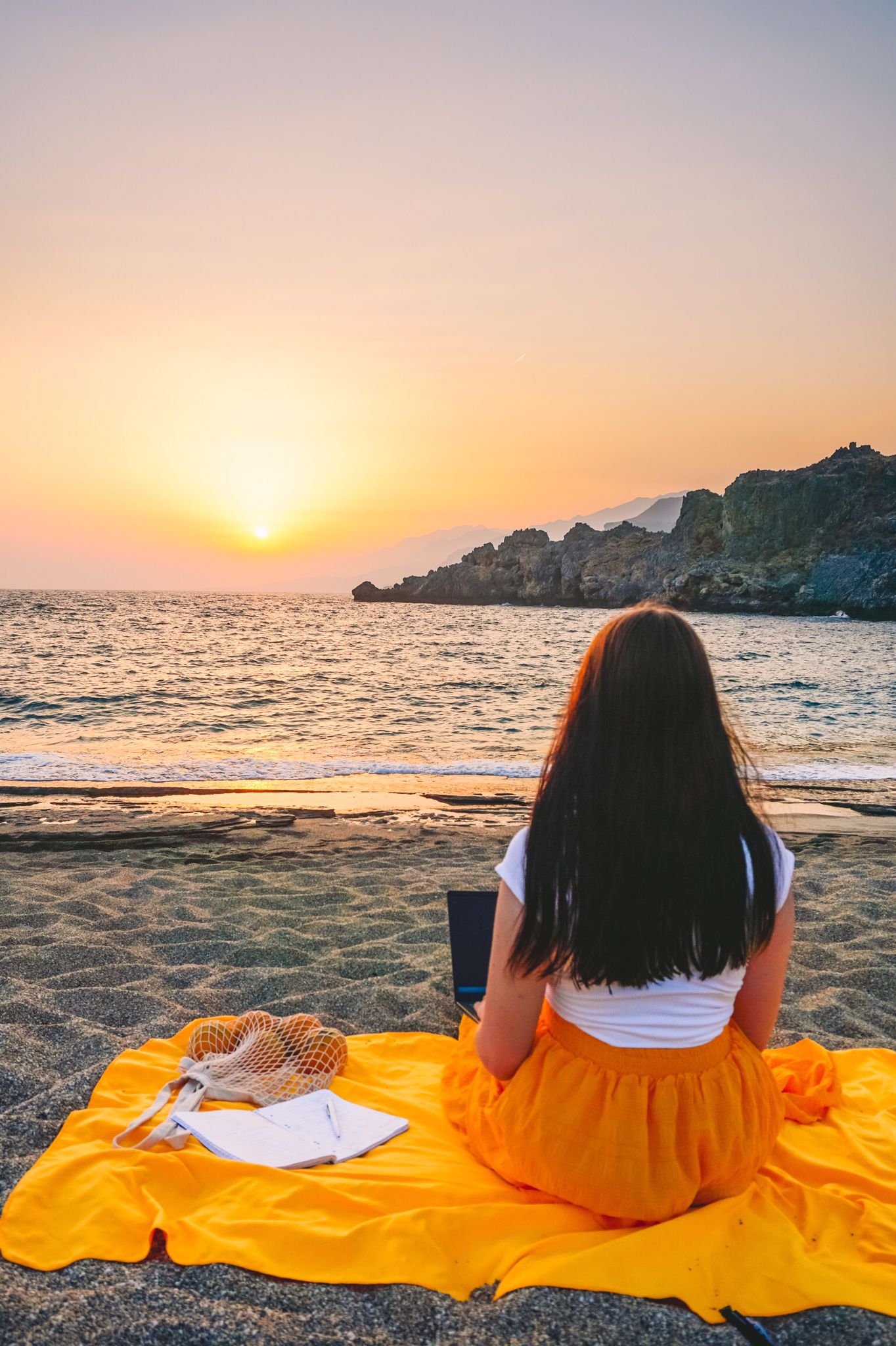 Anki sitzt mit Laptop bei Sonnenuntergang am Strand