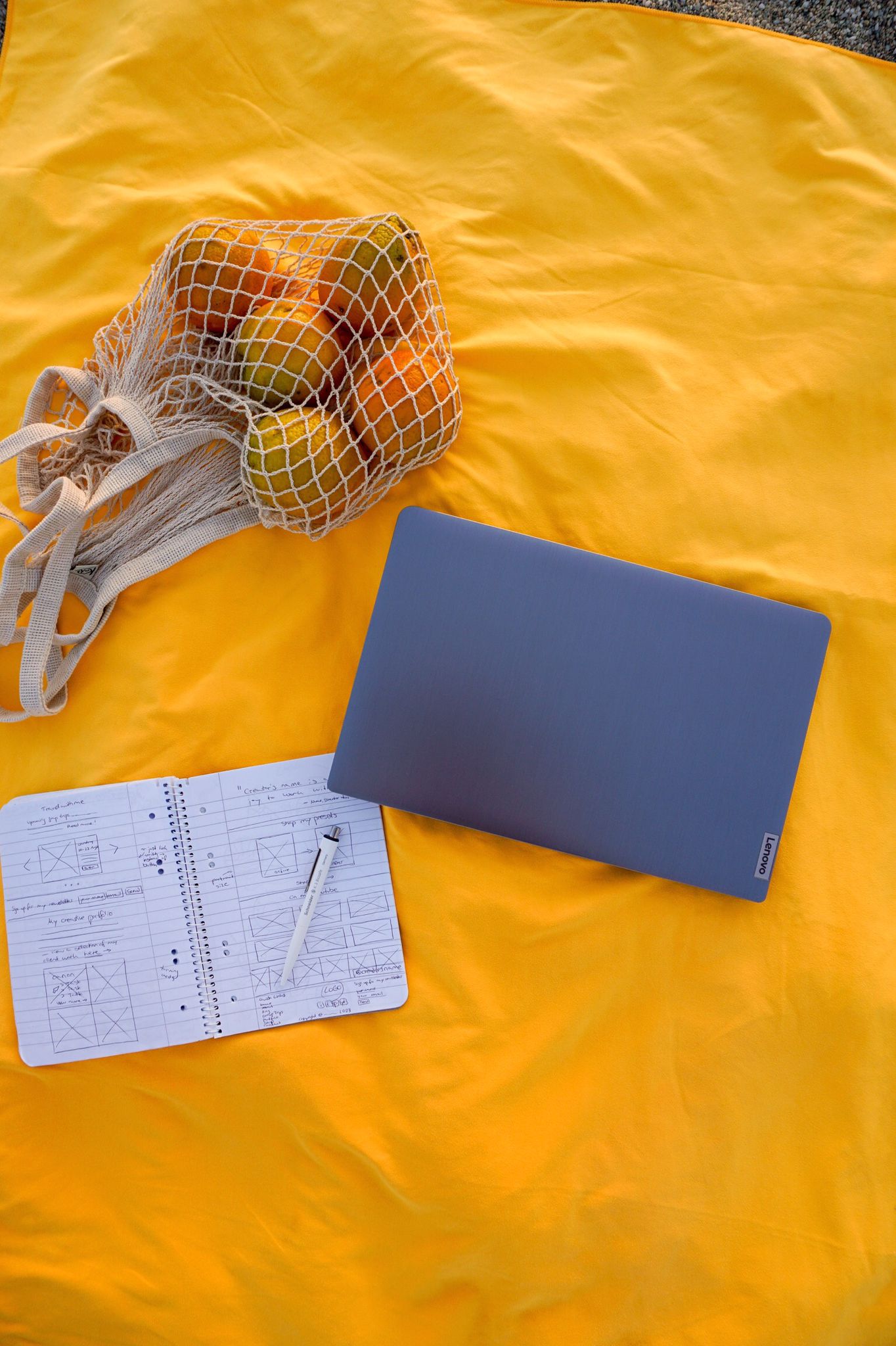 Laptop, bag of oranges & notebook on a yellow beach towel